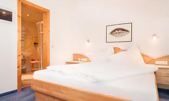 A cozy hotel room with a large bed and wooden interior. In the background, a bathroom is visible.