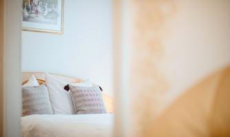 A cozy bedroom with a bed and several pillows. A painting hangs on the wall, and the room feels bright and welcoming.