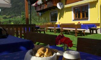 A hearty breakfast with sausage, cheese, eggs, and rolls on a table outdoors. In the background, you can see a yellow house with flower balconies and a beautiful blue sky.