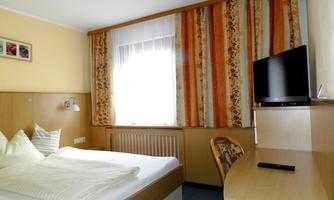 A cozy bedroom with a large bed and a desk. Windows with curtains provide daylight and an inviting atmosphere.