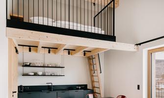 A modern room with an open living area and a small loft. The space has a minimalist style with a table and red chairs.
