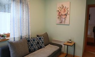 A cozy room with a gray sofa and a small table. A picture with floral motifs hangs on the wall.