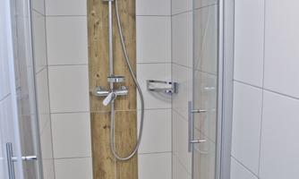 A modern shower with glass walls and wooden cladding. The white tile finish creates a clean and contemporary atmosphere.