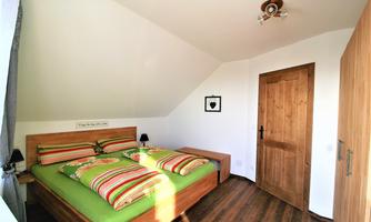 A cozy bedroom with a double bed and colorful bed covers. The room has modern wooden paneling and a bright, friendly atmosphere.