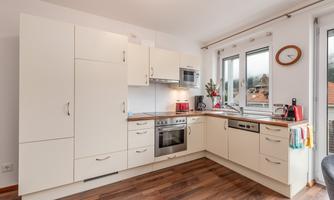 A modern kitchen with bright furniture and a wooden floor. Large windows let in plenty of light and create an inviting atmosphere.