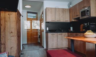 A modern kitchen with wooden cabinets and light walls. The table is made of wood and there are windows with a view outside.