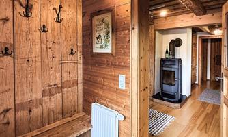 A cozy hallway with wooden walls and a wood stove. There is a bench and coat hooks on the wall.
