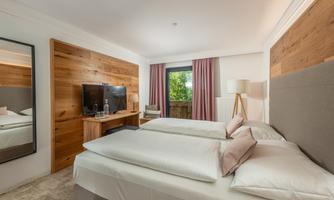 A modern hotel room with two single beds and a large window. The walls are partially clad in wood, and there is a television as well as a desk.