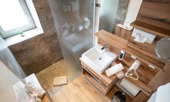 A modern bathroom with wooden shelves and a clear shower. The floor is made of wood and there is a large window opening for natural light.