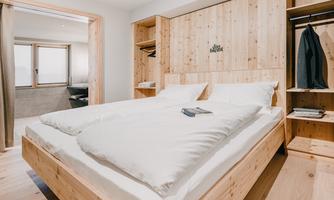 A modern bedroom with a large wooden bed and bright wooden interiors. The calm atmosphere is enhanced by large windows and minimalist furniture.