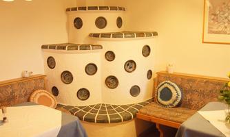A cozy tiled stove in a restaurant with round windows. Next to the stove are wooden-paneled benches.
