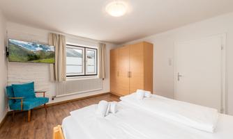 A simple room with two single beds and a large window. In the room, there is a television and a blue chair.