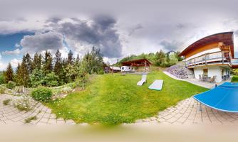 A picturesque holiday home with a large lawn and trees in the background. There are loungers and a blue sun umbrella in the garden.