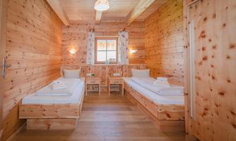 A cozy room with wood paneling and two beds. The room has a window with curtains and warm lighting.