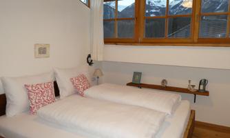 A cozy bedroom with a double bed and bright pillows. Through the windows, you can see the snow-capped mountains.