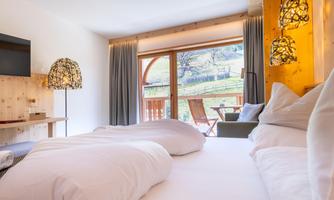 A modern room with two beds and wooden details. Large windows provide a beautiful view of nature.