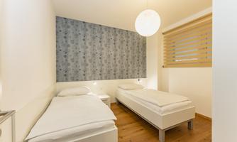 A cozy bedroom with two single beds and a modern design. The room has a bright atmosphere with a wallpapered wall and large windows.