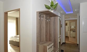 A modern hallway with a wooden wardrobe and space for coats. There is elegant lighting and a view of a bedroom.