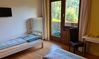 A simple bedroom with two single beds and a television on the wall. There is a balcony with a view of nature.
