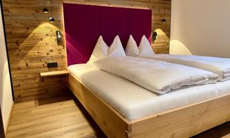 A cozy bedroom with a wooden bed and large white pillows. The wall is paneled with wood and has a striking pink headboard.
