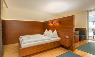 A modern bedroom with a wooden bed and two pillows. The room is bright and tidy, with a cozy seating area.