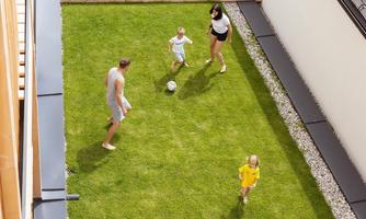 A family is playing soccer in the garden. There is a green lawn and sun loungers in the background.
