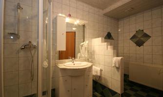 A modern bathroom with a shower, a sink, and a large mirror. The walls are covered with white tiles and the floor has an adjacent pattern.