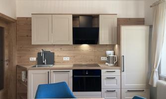 A modern kitchen with wooden paneling and white furniture. It includes a stove, a sink, and a refrigerator.