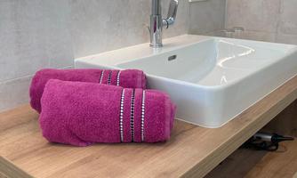 A modern bathroom with a sink and high-quality fittings. Pink towels are placed on a wooden shelf.