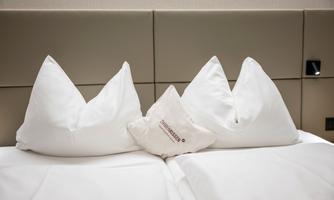 A cozy bed with three decorative pillows in white. The pillows are neatly arranged and create an inviting atmosphere.