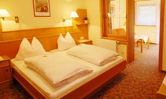 A cozy bedroom with a double bed and large cushions. The room has warm lighting and a view of an adjacent living area.