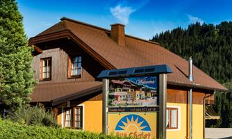 A charming chalet with an inviting "Welcome" sign. Surrounded by green trees and hills.