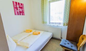A simple bedroom with two beds, fresh towels, and a chair. The window brings natural light into the room.
