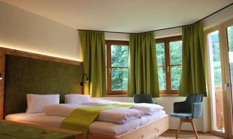 A bright and modern room with large windows and green curtains. There is a comfortable double bed and a cozy armchair.