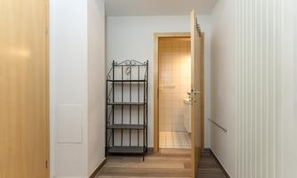 A bright hallway with an open door to a bathroom. A black shelf stands against the wall.