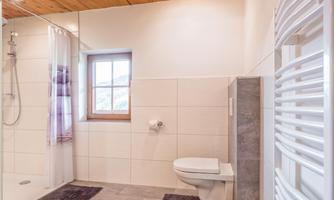 A modern bathroom with a shower and toilet. The room features light tiles and a wooden ceiling, which creates a warm atmosphere.