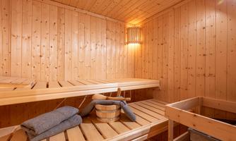 A relaxing sauna room with wooden shelves and soft lighting. Towels and a bucket are ready for a soothing break.