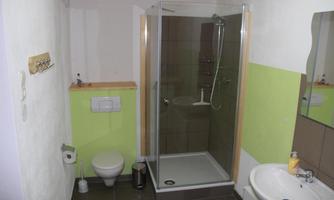A modern bathroom with a shower cabin and a sink. The walls are designed in neutral colors, with a green accent.