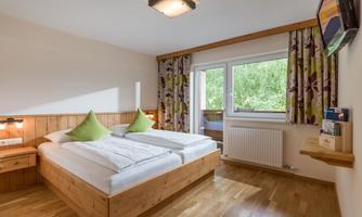A cozy bedroom with two single beds and colorful cushions. The room has large windows that let in plenty of natural light.