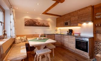 A cozy kitchen in rustic style with wooden shelves and modern equipment. A round table with benches invites you to linger.