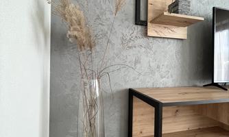 An elegant glass vase with dried flowers stands in a modern apartment. In the background, there are wall shelves with plants and a wooden cabinet.