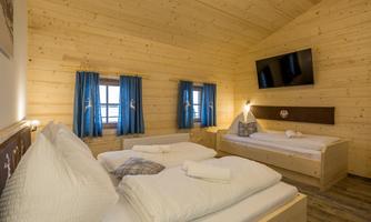 A cozy room with wooden paneling and blue curtains. There are two beds and a TV on the wall.