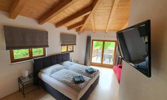 A modern bedroom with a double bed and a flat-screen TV. Large windows let in plenty of daylight and offer a view outside.