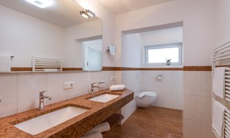 A modern bathroom with two marble sinks and a clear, bright color scheme. The space is well-lit and offers a pleasant atmosphere.