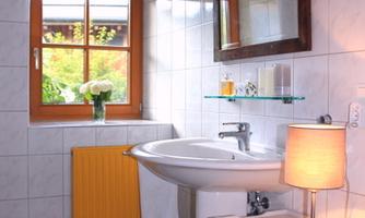 A cozy bathroom with white tiles and a large window. A sink, a mirror, and a lamp create an inviting atmosphere.