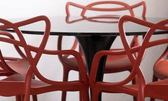 A round table with a black surface and red chairs. The chairs have a modern, playful design.