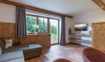 A modern living room setup with a cozy sofa and large windows. The room has a beautiful view of the green landscape outside.