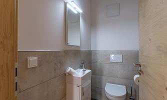 A modern bathroom with simple tiles and a sink. The walls are light-colored and there is a large mirror.
