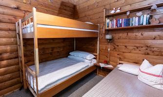 A simple room with a bunk bed and a single bed. The wall features bookshelves and wooden paneling.