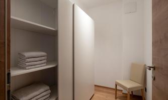 A bright room with a white shelf containing neatly folded towels. A simple chair stands next to it and the floor is made of wood.